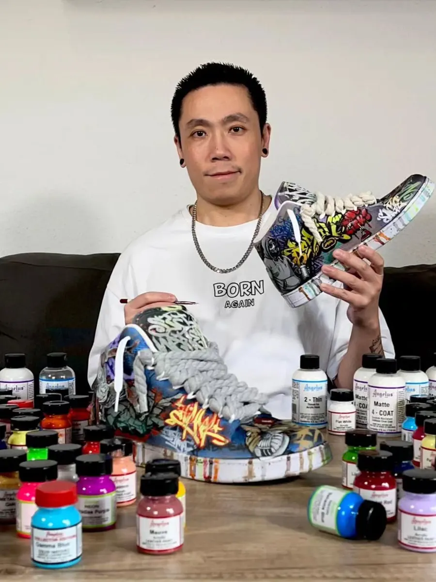 Steven hält einen handbemalten Custom-Sneaker vor seinen Farbflaschen